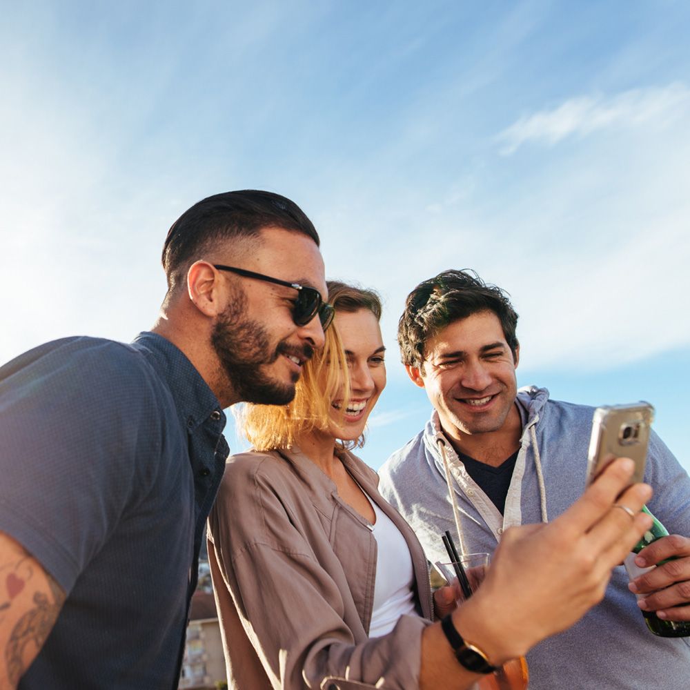 Three friends looking at a phone and smiling Three friends looking at a phone and smiling
