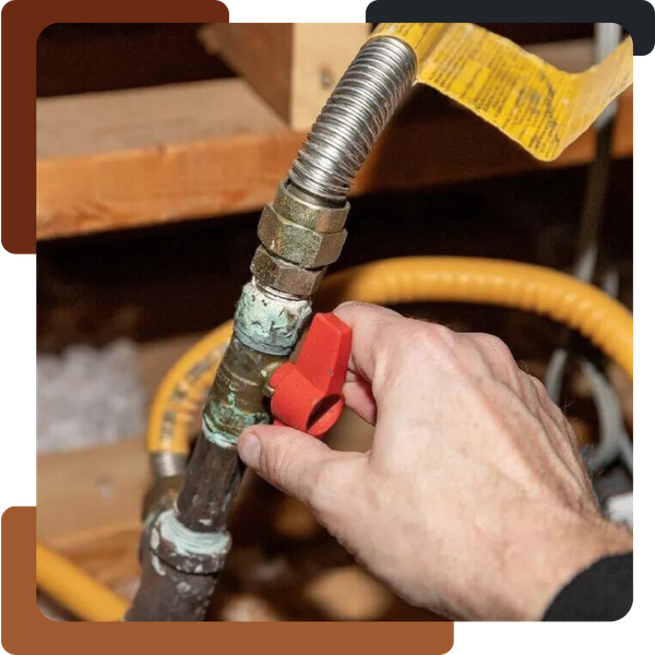 A close-up of a hand turning a red handle on a gas shut-off valve connected to an old copper or metal pipe and a newer yellow flexible gas line.