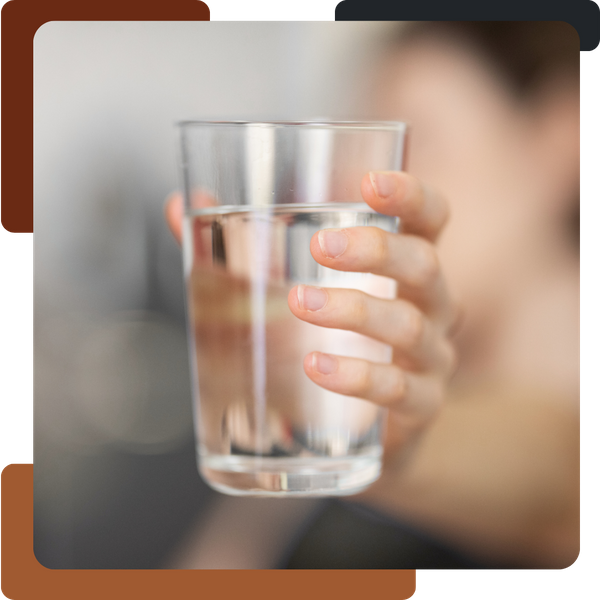 A blurred, close-up image of a person holding a clear glass of water toward the camera.