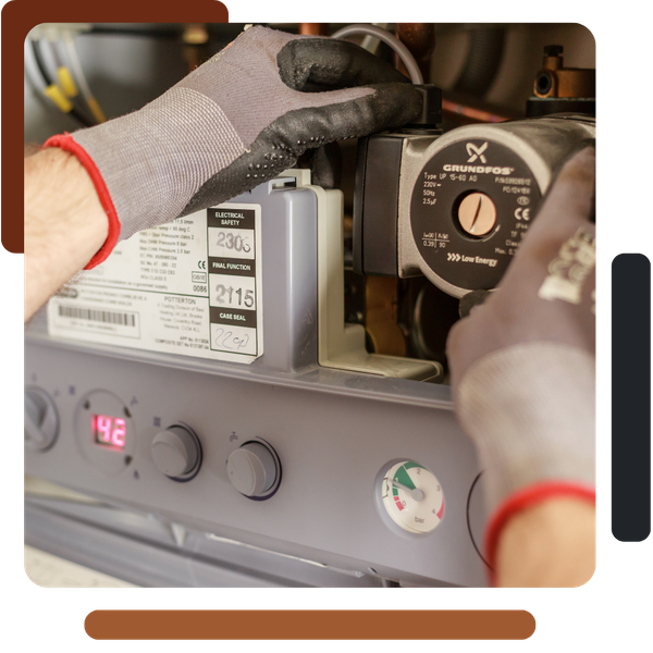 A close-up shot of a technician wearing work gloves adjusting or inspecting the pump and controls of a boiler or heating system.