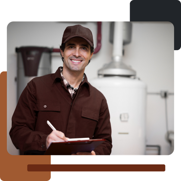 A smiling male plumber or technician, wearing a brown uniform jacket and cap, stands indoors in a utility room with white water heaters visible in the background, holding a clipboard and pen.