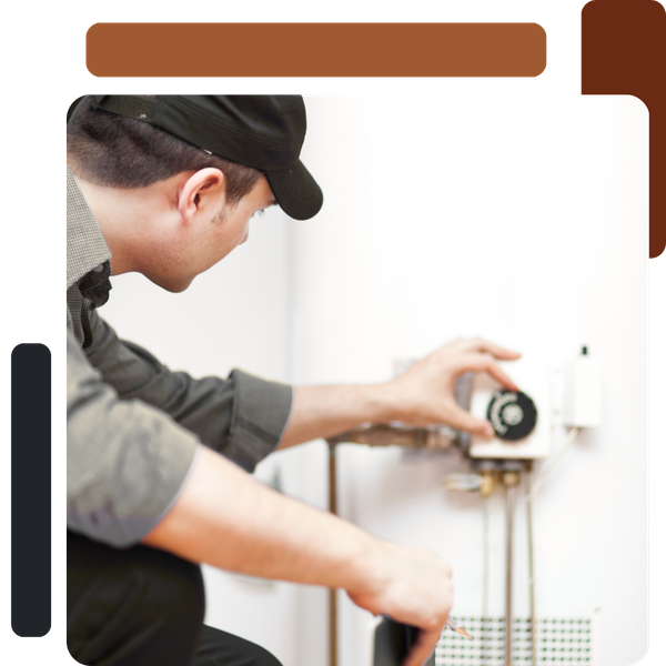 A plumber or technician, wearing a dark cap, crouches to adjust the thermostat or control panel on the side of a white residential water heater.