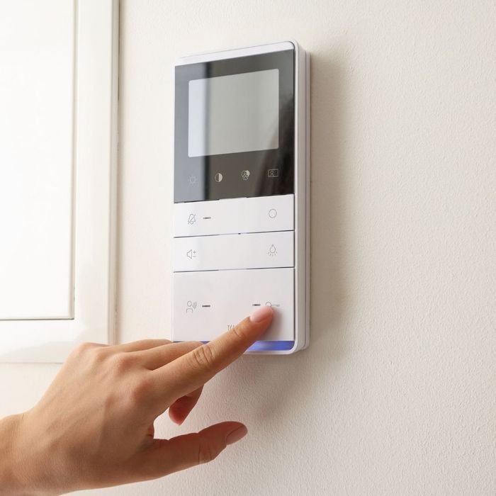 A person’s hand adjusting a sleek, modern smart thermostat mounted on a clean, neutral-colored interior wall.