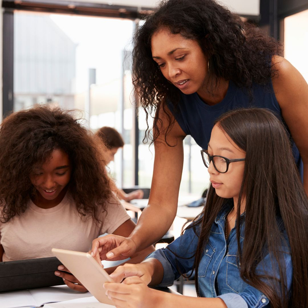 teacher looking at tablet with 2 students