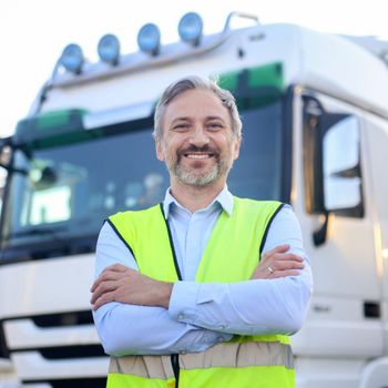 Truck driver in reflective vest smiling in front of truck