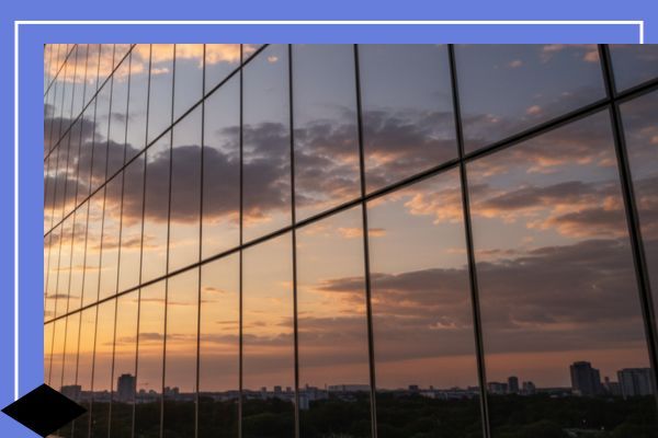 The glass facade of a modern high-rise building reflecting a vibrant sunset sky with hues of orange and pink, emphasizing the mirror-like exterior and privacy provided by the window film.