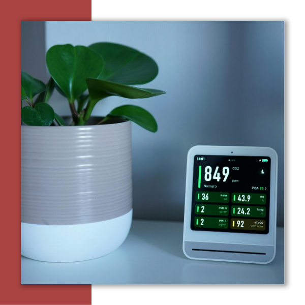 An indoor air quality meter next to a house plant.