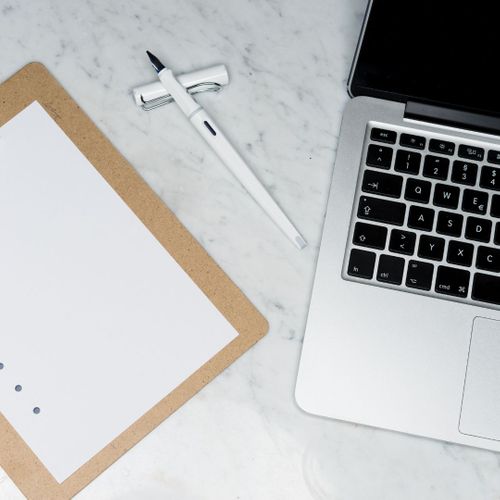 Laptop, clipboard, and pen on marble desk.