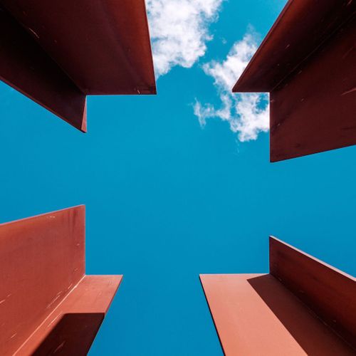 Upward view of red metal beams against blue sky