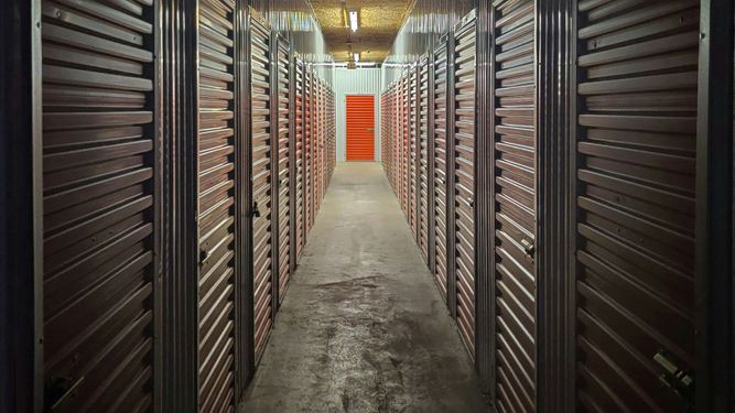 Narrow hallway of indoor storage units, orange door at end.