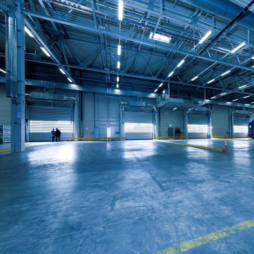 Large, empty warehouse interior with overhead lighting and open bays