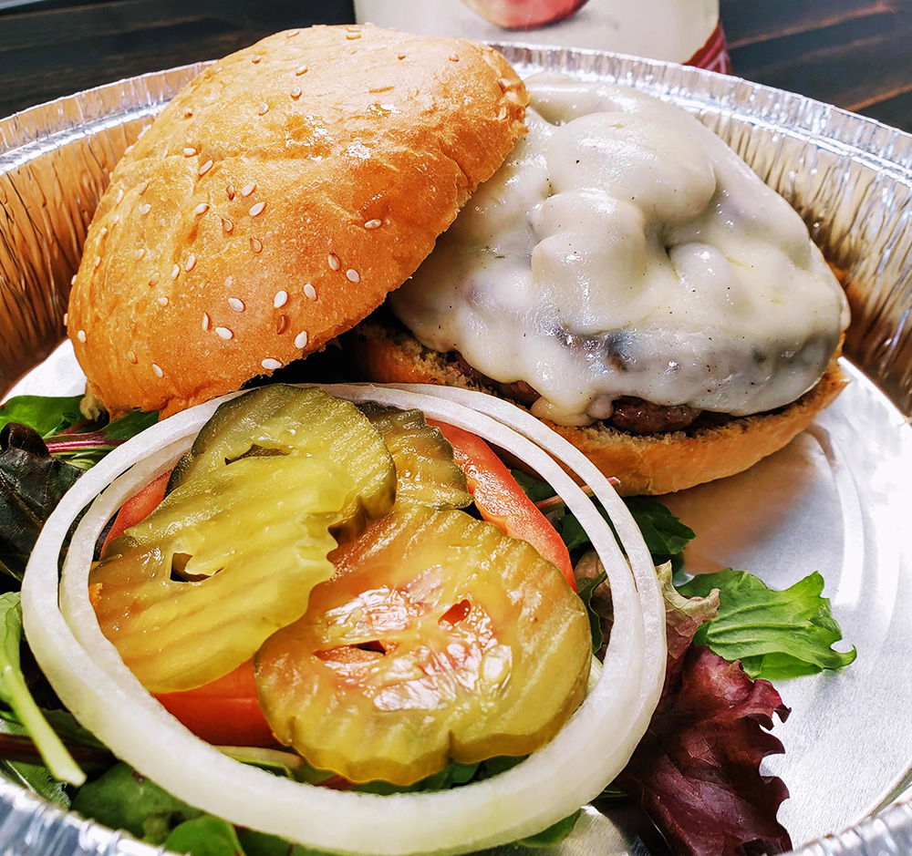 Hamburger with gravy, lettuce, tomato, pickles and onion on a sesame seed bun