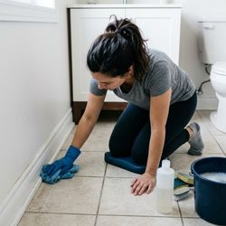 Image of a woman cleaning bathroom baseboards