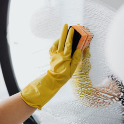 a gloved hand wiping a mirror covered with a cleaning solution with a sponge