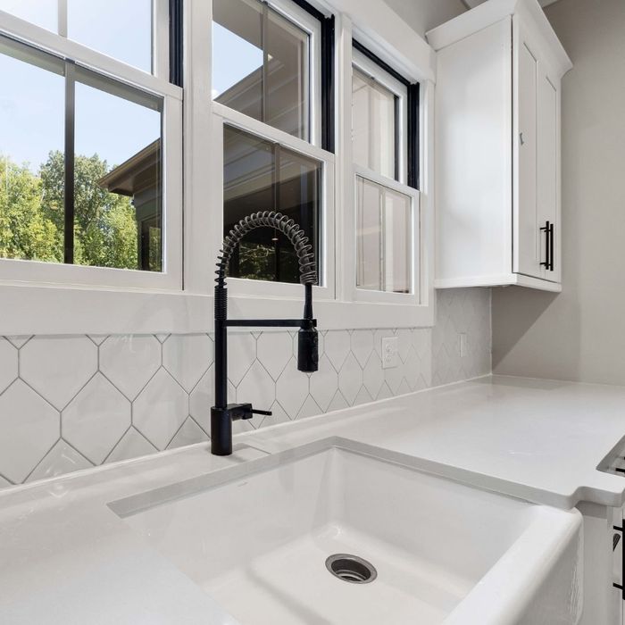 Modern kitchen with a white farmhouse sink, black pull-down faucet, and geometric tile backsplash.