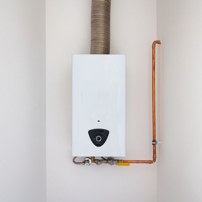 White tankless water heater installed on a wall with copper pipes.