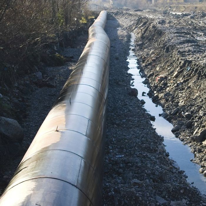 Large metal pipeline running along a trench with water, surrounded by dirt and rocks.