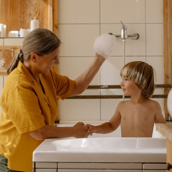 grandmother holds up bubbles with kid in bathtub 
