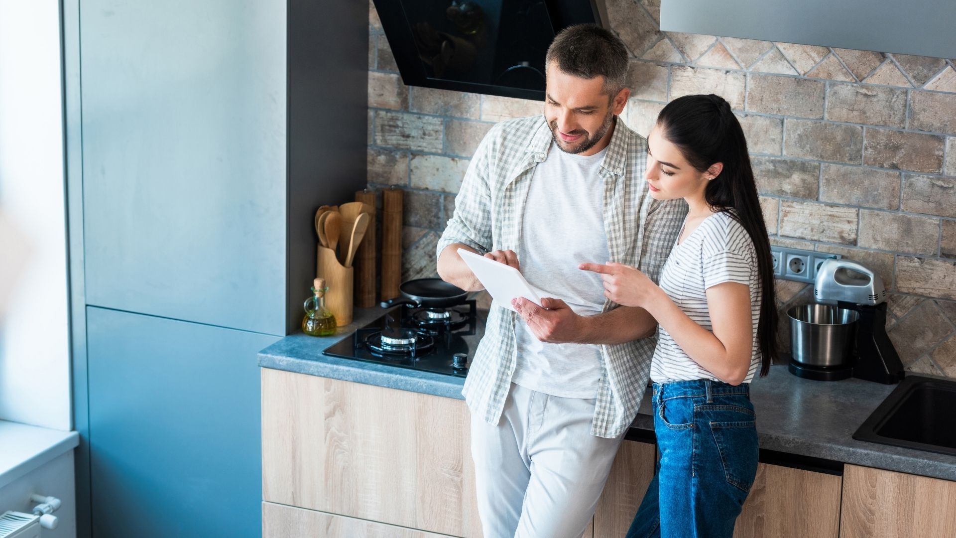 smiling couple standing in kitchen looking at tablet smiling couple standing in kitchen looking at tablet
