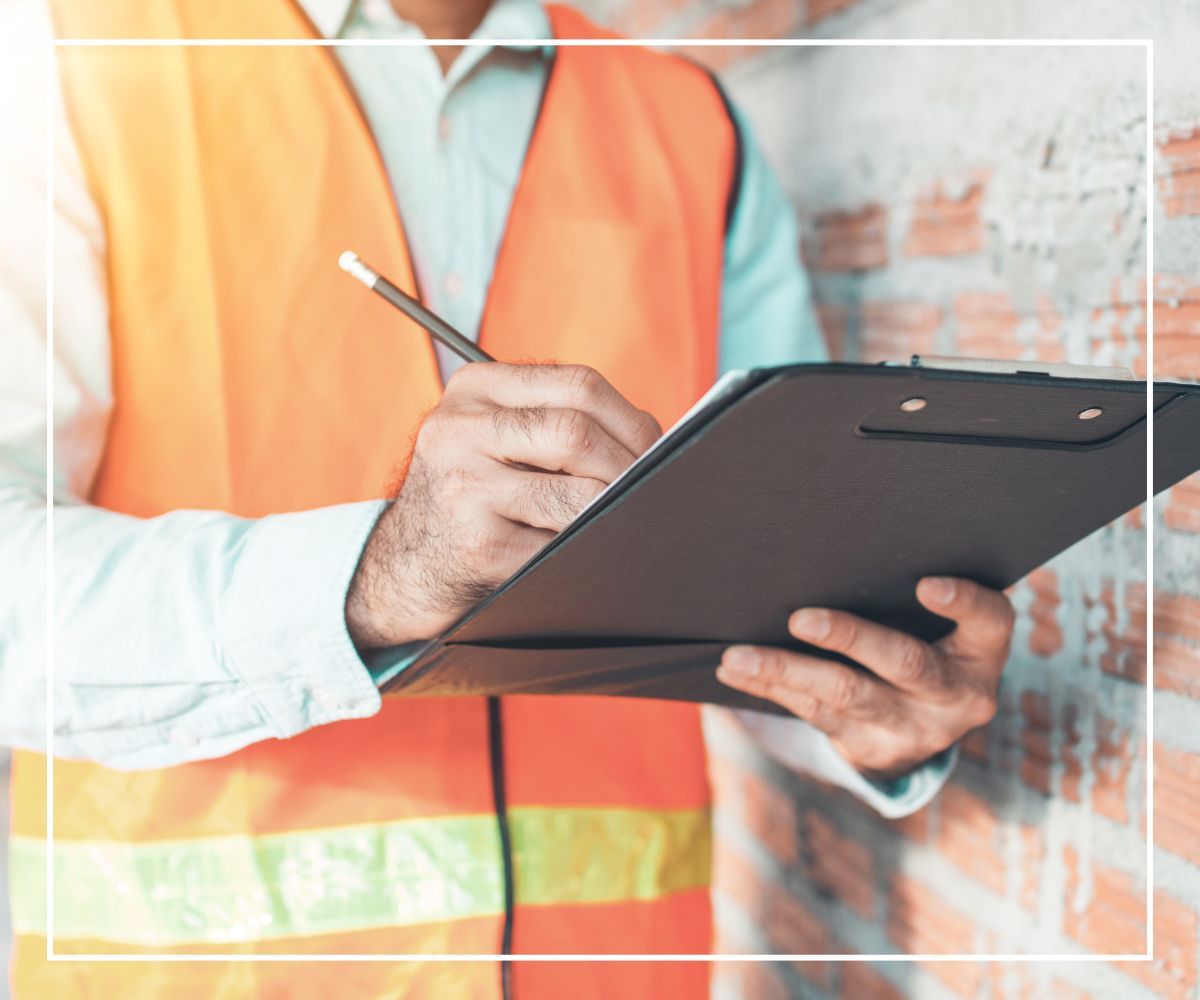 A worker in a safety vest writing on a clipboard
