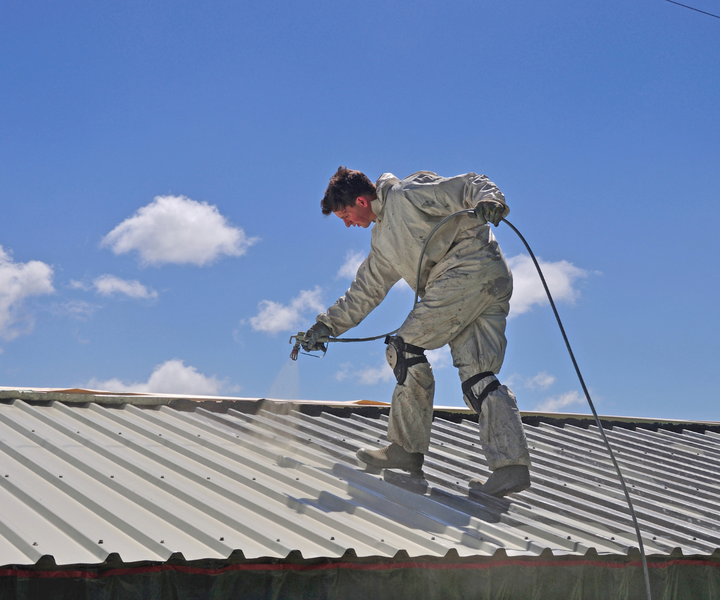 A commercial roofing contractor uses a spray gun to apply silicone spray to a roof