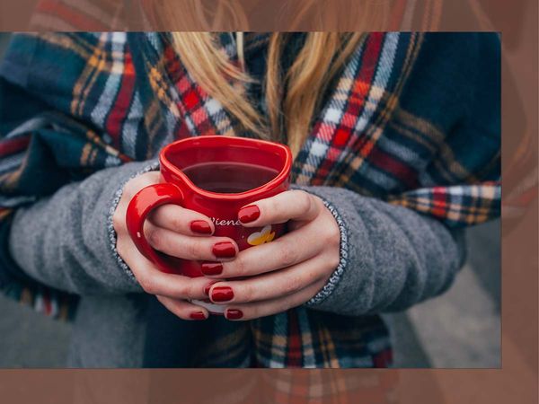 A woman wearing a plaid scarf holding a warm beverage. 