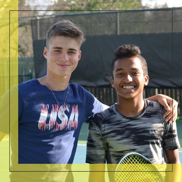two teen boys smiling together on a tennis court