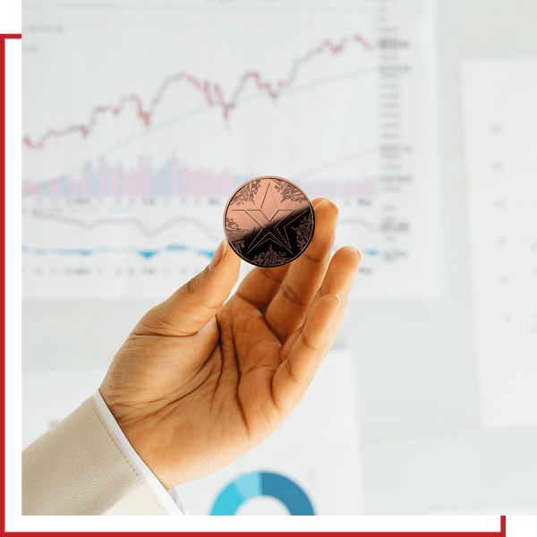 A hand holding a physical copper TEXITcoin against a backdrop of financial growth charts.