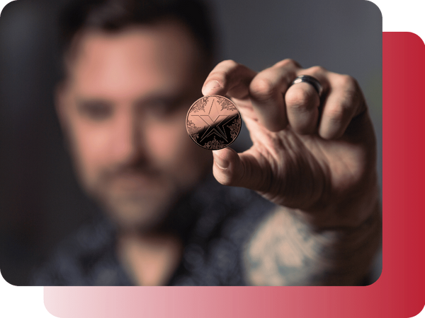 A man holding a copper TEXITcoin up to his eye, inspecting it closely.