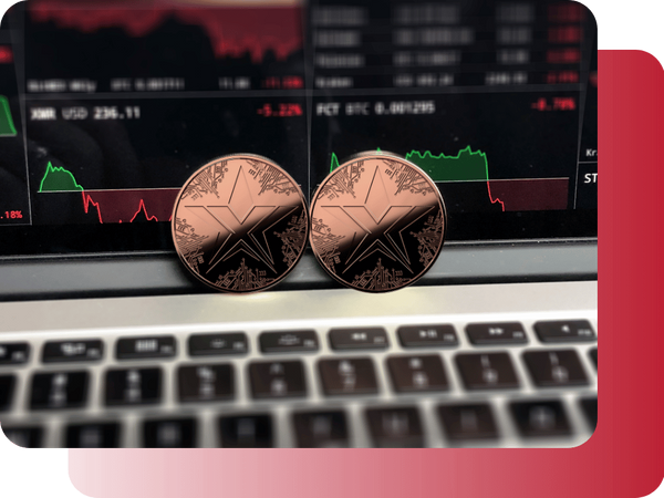 Two physical TEXITcoins placed on a laptop keyboard with live trading charts visible on the screen.