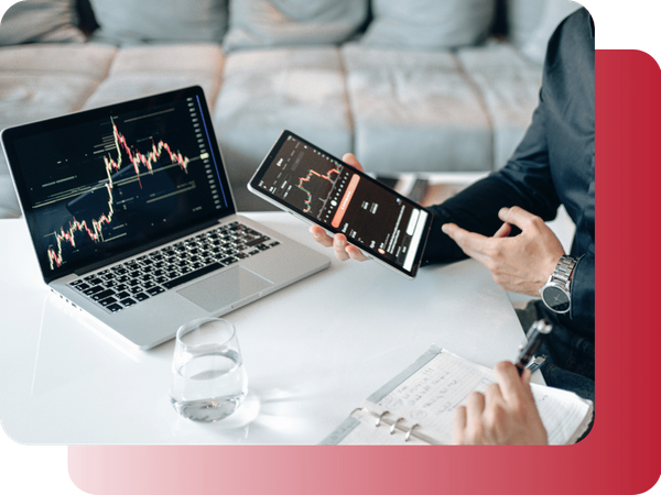 A business professional reviewing market data on a tablet and laptop in an office setting.