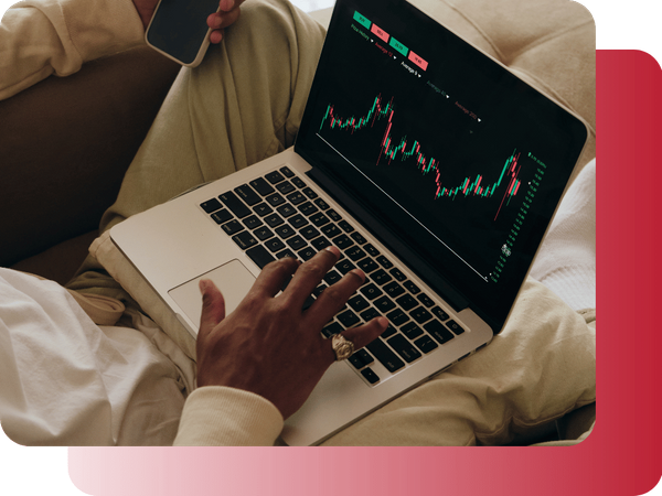 A person sitting on a couch working on a laptop while checking financial data on a phone.