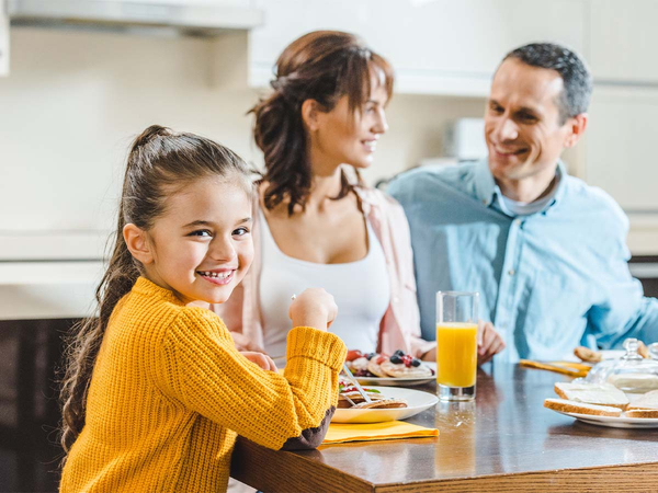 A young girl in yellow at the breakfast table with parents