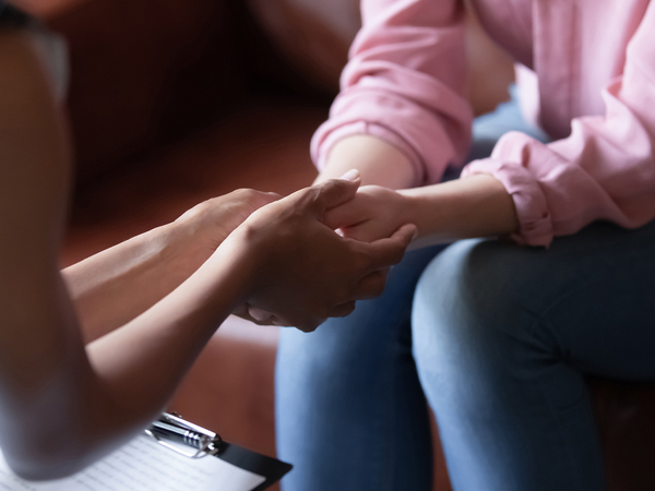 Two people sitting down, with a woman holding the hands of another person. 