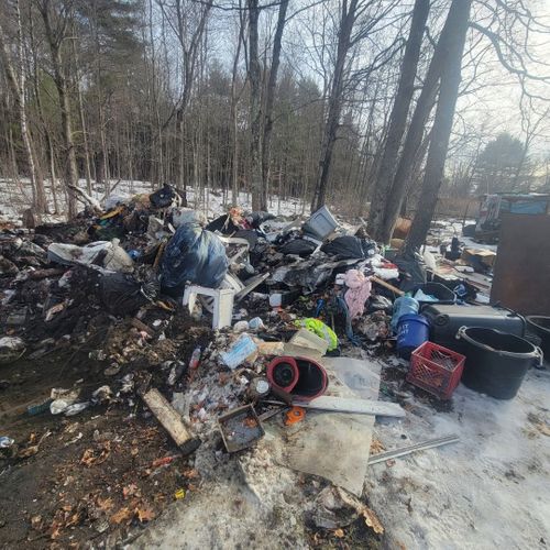 Pile of debris and garbage in a wooded outdoor area.