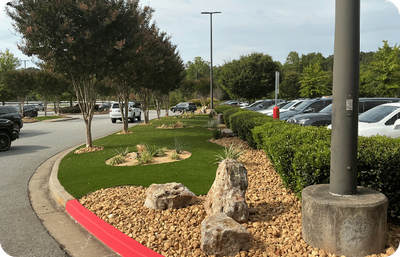 Landscaped median in a parking lot with artificial turf, rocks, and plants