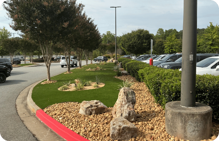 Landscaped median in a parking lot with artificial turf, rocks, and plants