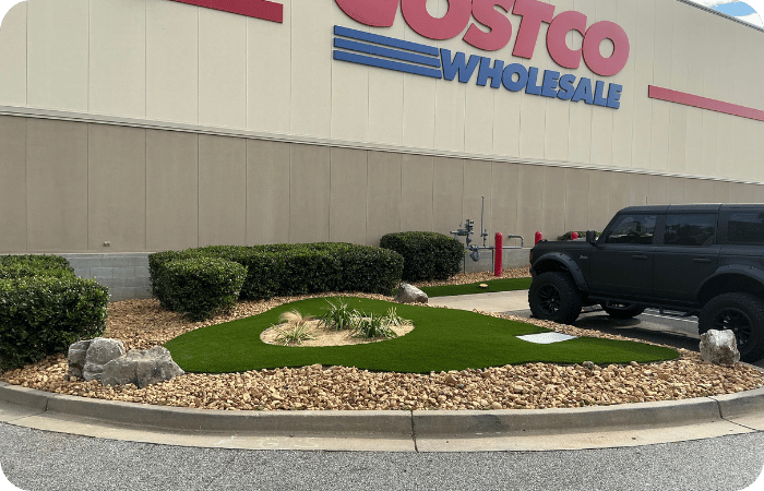 Landscaped area with artificial turf and rocks in front of a Costco Wholesale building