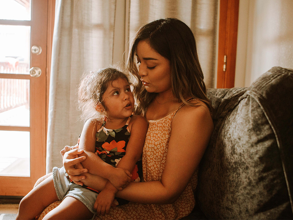 Latina woman and her daughter sitting on a chair in their home