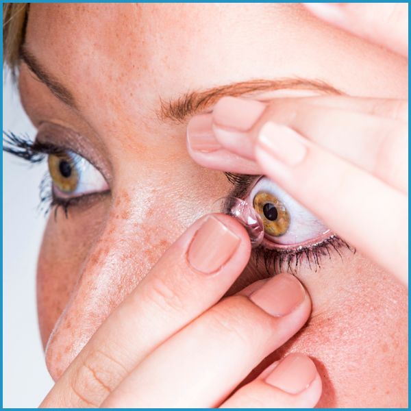 person inserting contact lens into eye