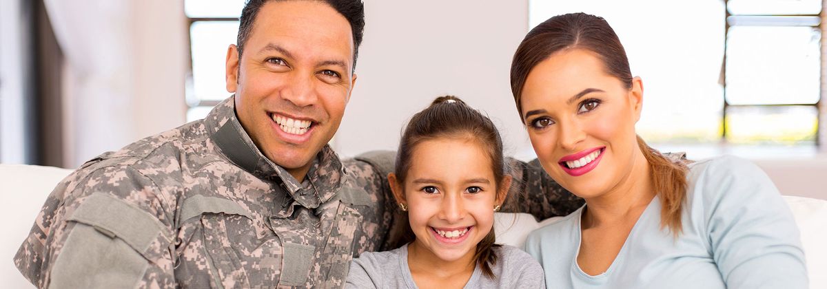 father in uniform sitting with wife and young daughter