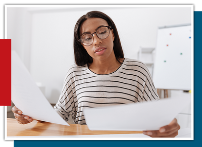 Serious pleasant young woman sitting at the table and looking at the documents while working