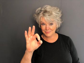 Woman with styled gray hair giving the okay sign with her fingers after a hair styling appointment at THE LONDONER in Hermosa Beach.