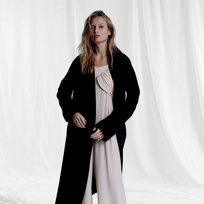 Woman in front of a white backdrop wearing a gray jumpsuit and black robe.