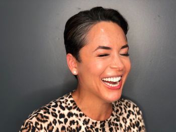 Laughing woman in an animal-print top smiling after having her short black hair styled in THE LONDONER's outdoor hair salon in Hermosa Beach.
