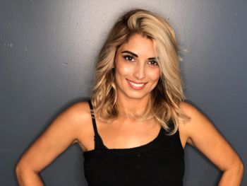 Woman with highlighted brown hair smiling in front of a gray background at THE LONDONER in Hermosa Beach.