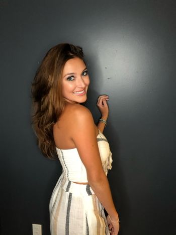 Woman in a white and gray dress smiling while standing in front of a gray background at THE LONDONER in Hermosa Beach.