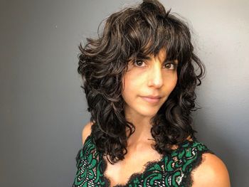 Woman with long brown hair looking into the camera while wearing a green and black top at THE LONDONER's Hermosa Beach hair salon.