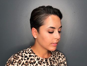 Woman with a leopard-print top and short black hair standing in front of a gray background at THE LONDONER's Hermosa Beach hair salon.