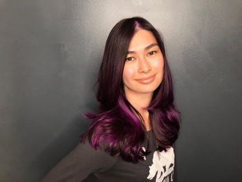 Woman with brown and purple hair wearing a black shirt standing in front of a gray background at The Londoner's South Bay hair salon.